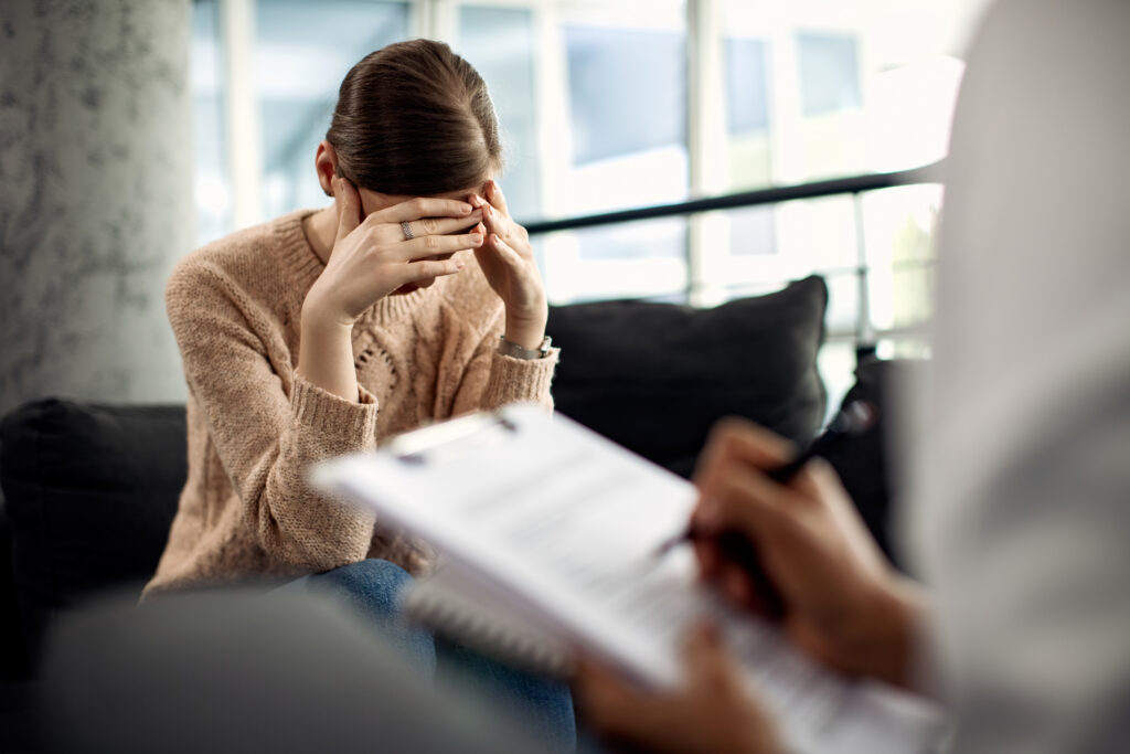 A person sits on a couch looking at papers with hands on their face.