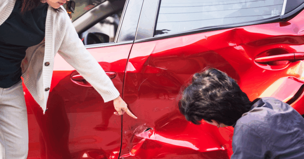 A person points to damage on the red body of a car.