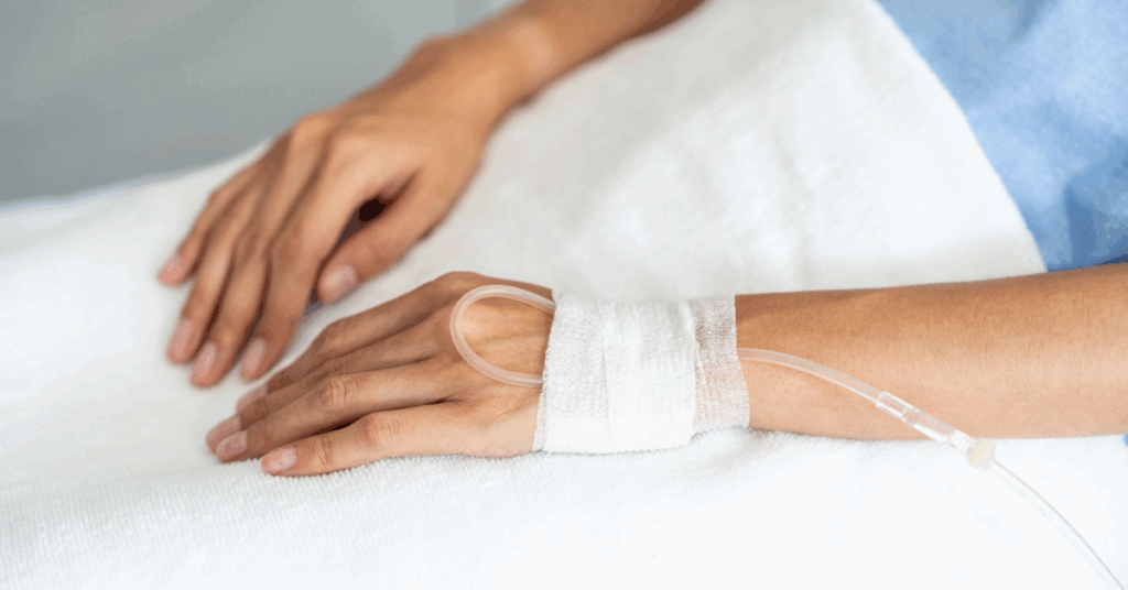 Hands rest on a white surface with a wrist bandage and medical tube.
