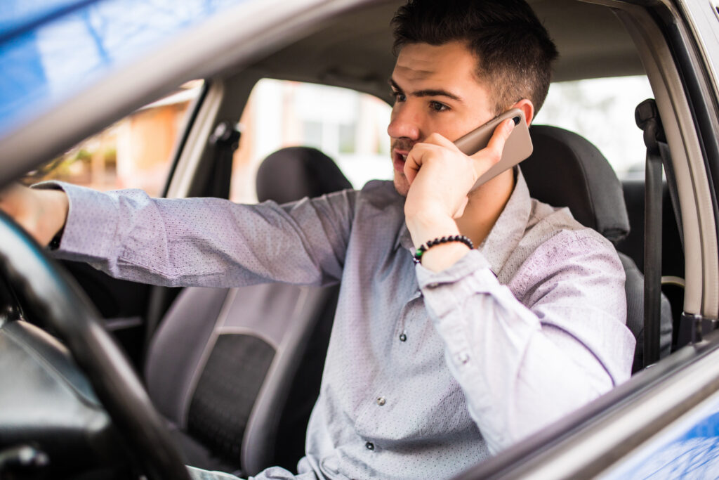 A man talks on a phone while sitting in a car.