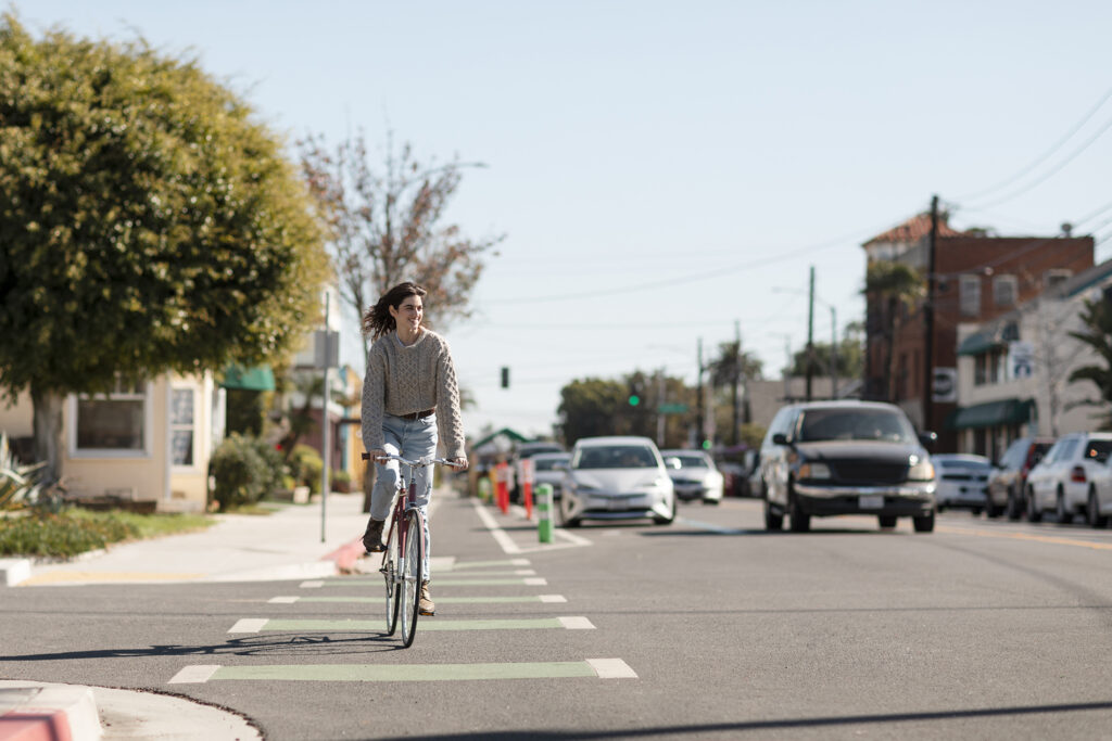 A woman rides a bicycle down a residential street with cars in the background.