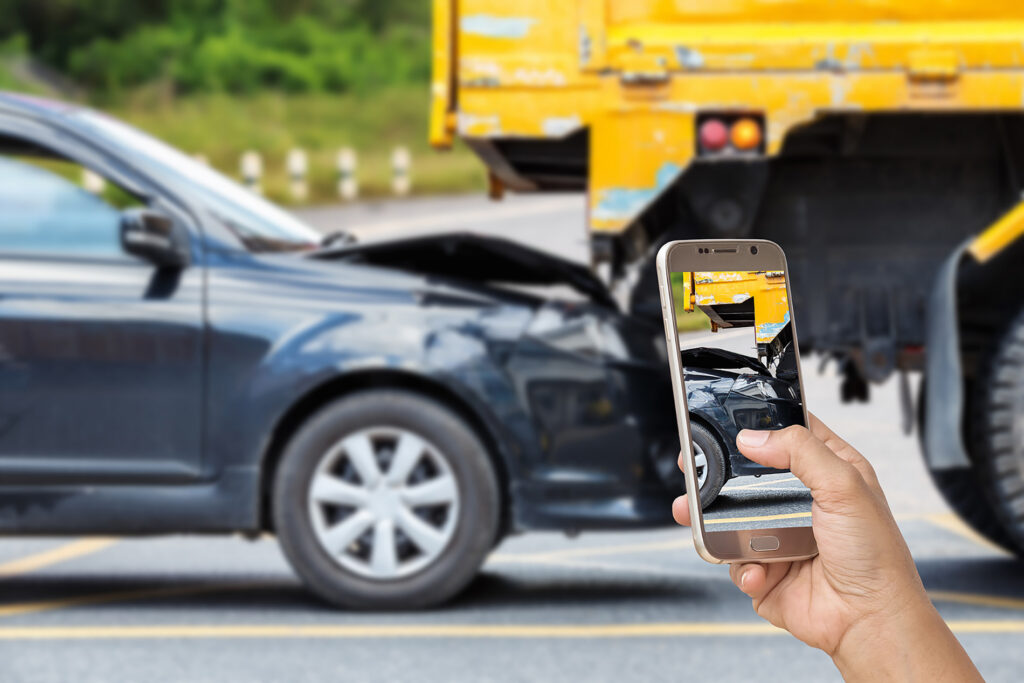 Hand holds a phone showing a dark car and a yellow truck.