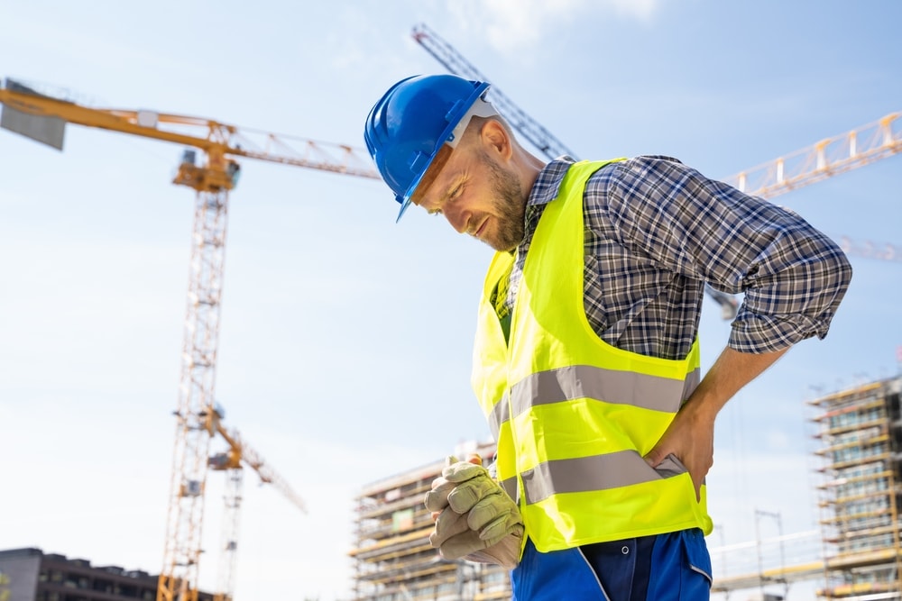 Closeup of construction worker holding their back after sustaining an injury