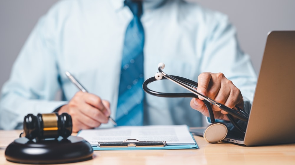 Personal injury lawyer sitting at a desk with a computer, gavel and stethoscope beside him