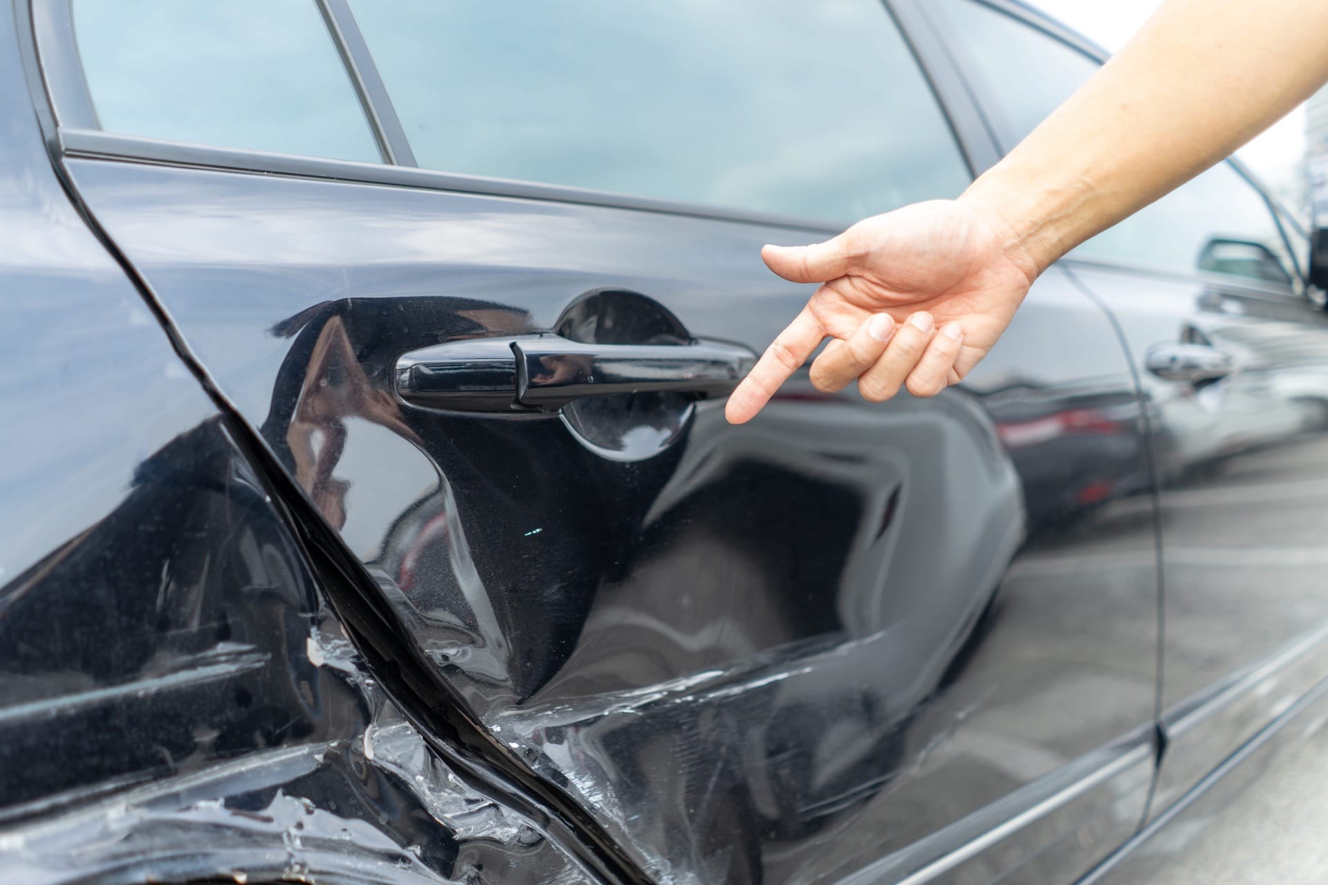 Photo of person pointing to a damaged car