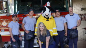 Receptionist Pam posing with GVL firefighters and Chik-fil-A mascot for International Firefighters Day